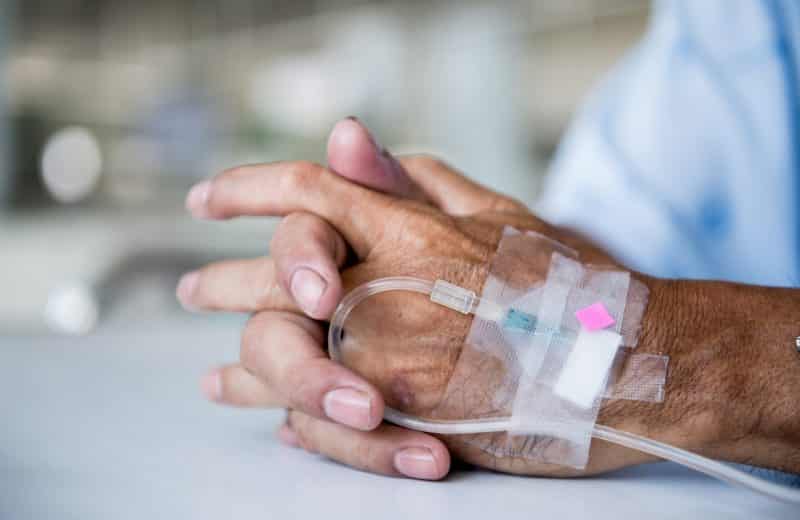 Hands of an older person in the hospital with an IV drop in