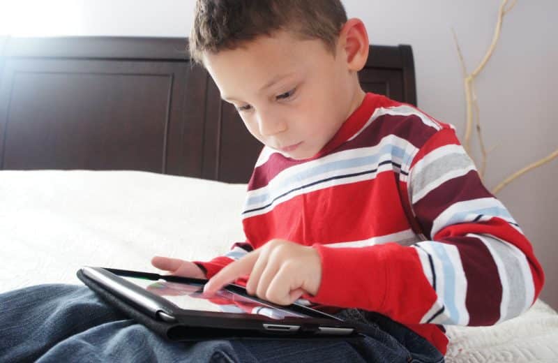 Young boy in striped red shirt looking down and playing with iPad