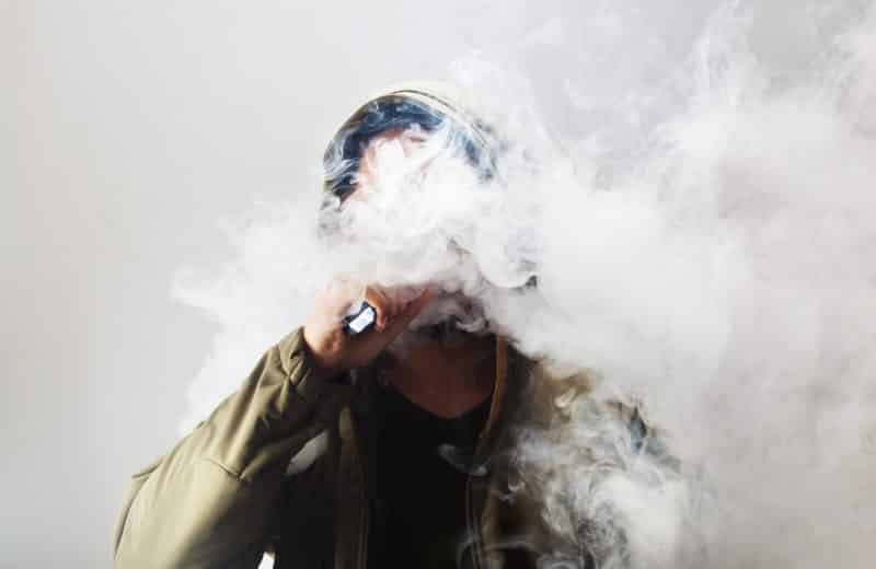 Male wearing hood, using electronic cigarette; face covered in smoke