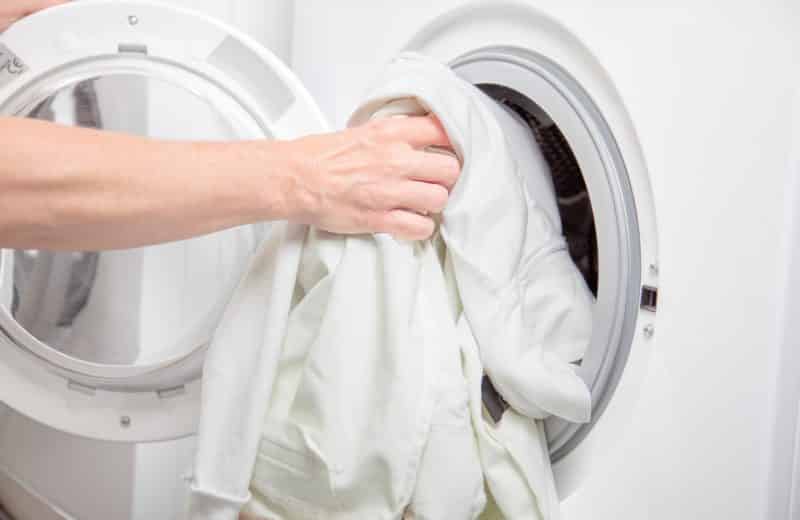 Hand putting white sweatshirt into washing machine
