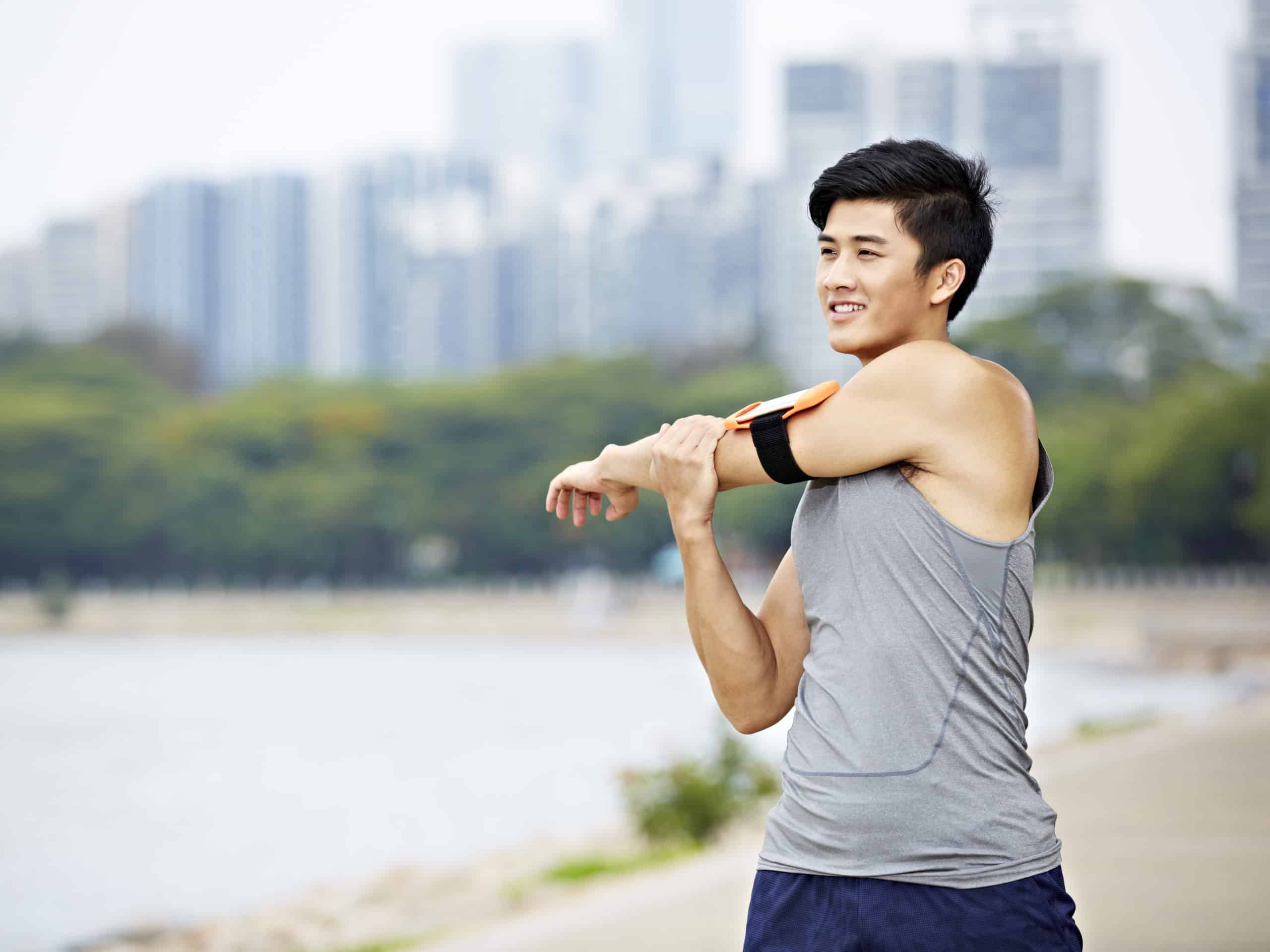 Young male, asian jogger stretching arms before running