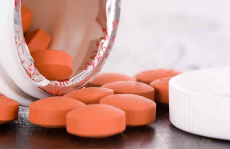 Bottle of ibuprofen open and on side on table with pills spilling out