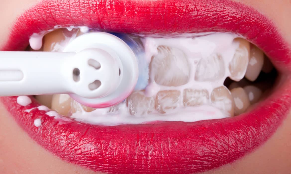 Woman with lipstick on protecting against periodontal disease by brushing teeth with electric toothbrush; closeup on mouth