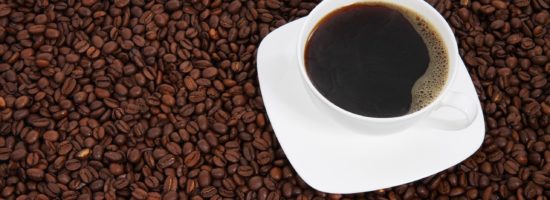 A cup of coffee in a white mug sitting on top of lots of coffee beans