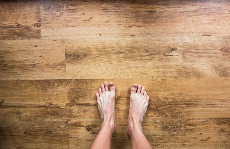 Feet without corns and calluses shot from above and standing bare on wooden floor.