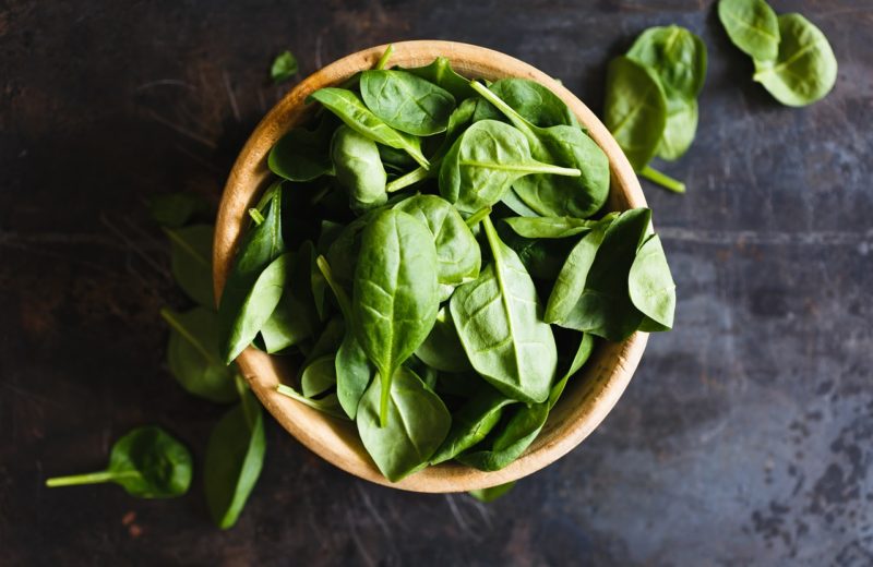 A bowl of spinach, an example of a food rich in vitamin e, shot from above on a slate table