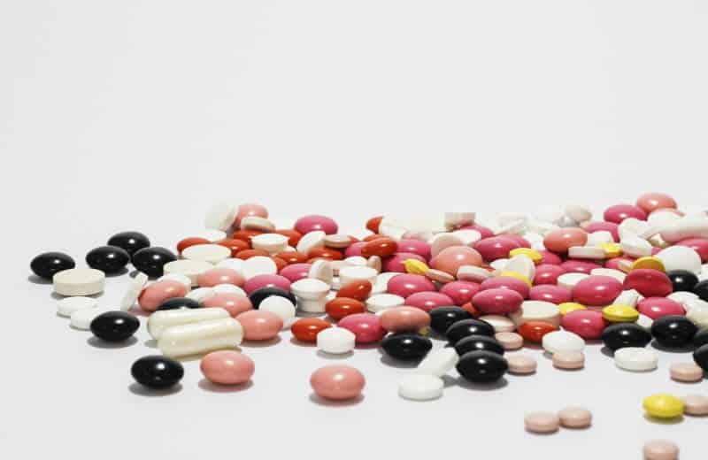 Can genetic testing help predict medication side effects? Image shows pile of various types and colors of pills on plain white background.
