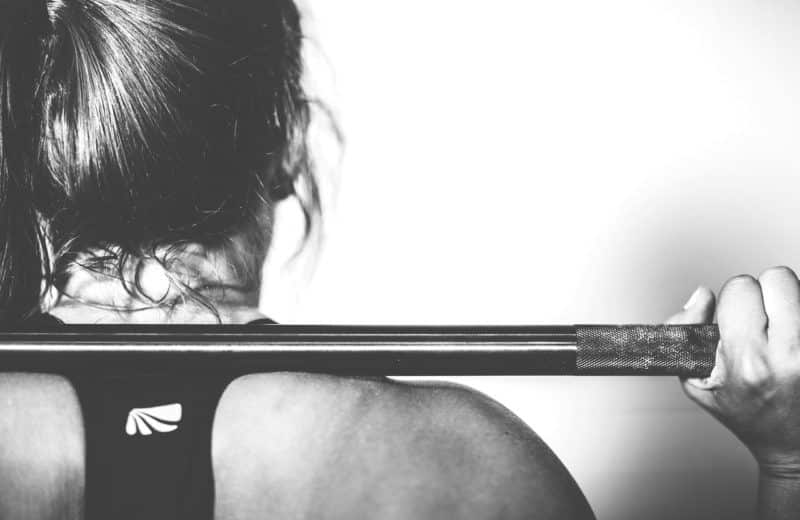 Power training: shot from behind of young woman with ponytail holding barbell on her shoulders.