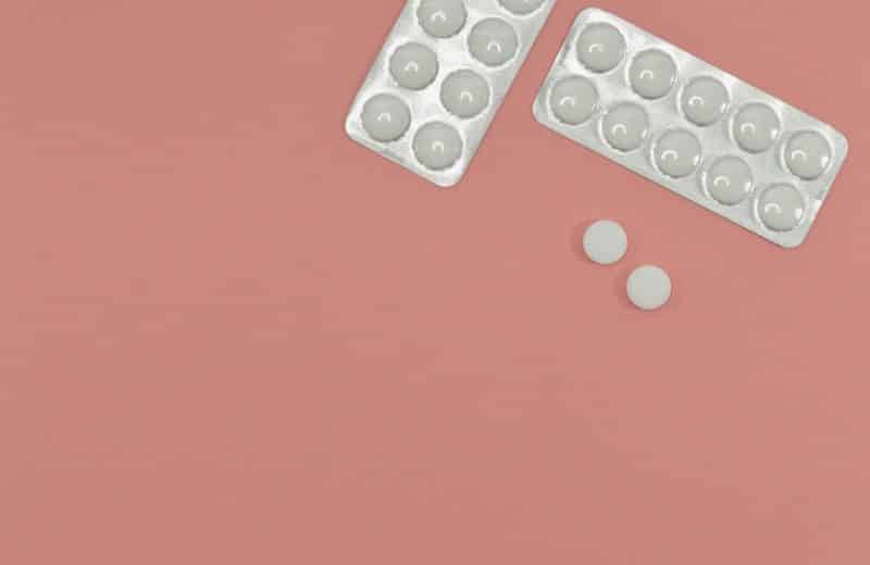 Statin drugs: Image of two packs of white pills on pink background, with two pills outside of pack