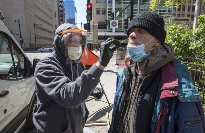 Koruba (left) tests an unsheltered person for Covid-19. He estimates he has administered over 20 tests to Chicago’s homeless, all negative. Photo by Lloyd DeGrane