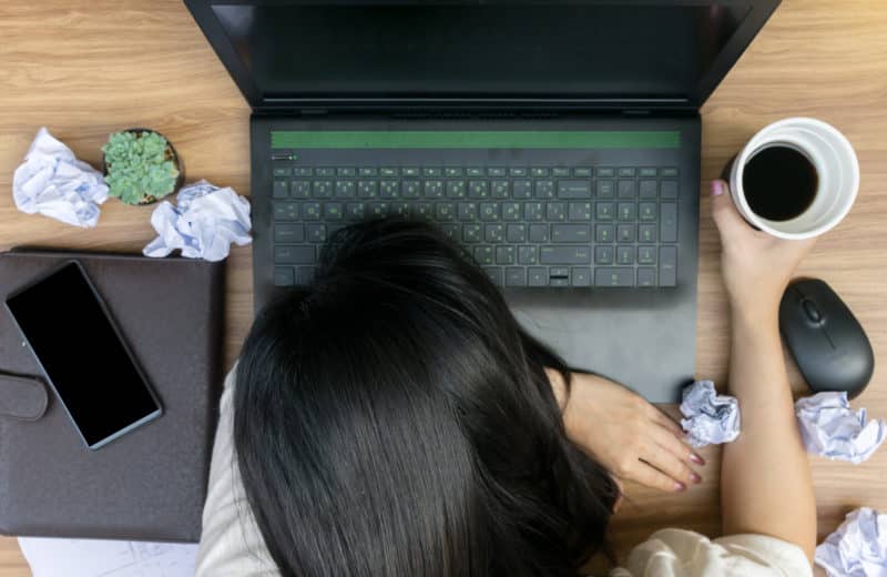 Perfectionism Woman hunched over laptop with crumpled balls of paper surrounding