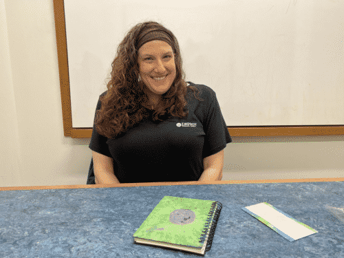 Angela Nino of Improv Therapy Group sits at a table with a green notebook.