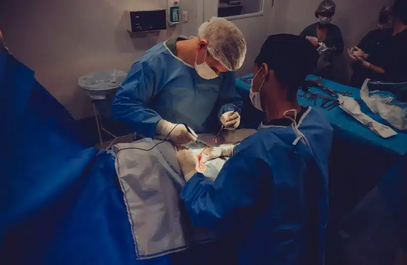 Two healthcare providers in blue scrubs operate on a patient in the OR.