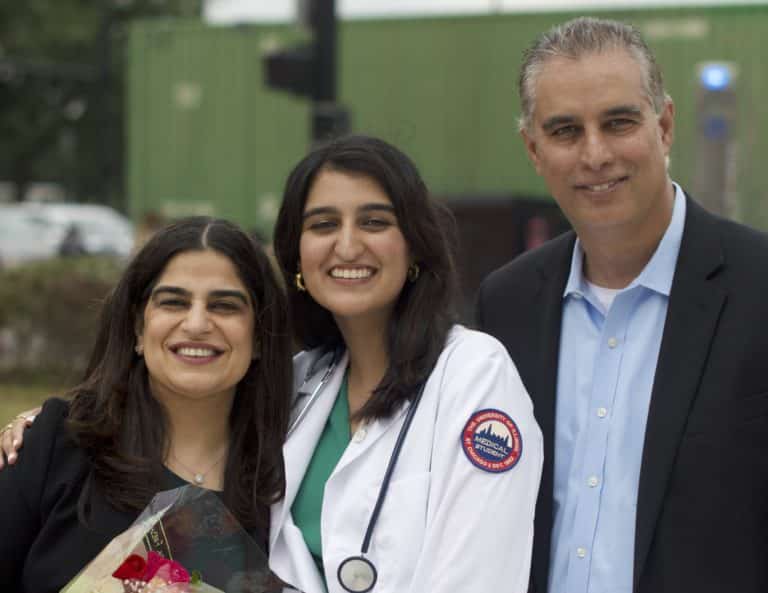 Medical student Hana Ahmed smiles, standing between her parents, at a White Coat Ceremony