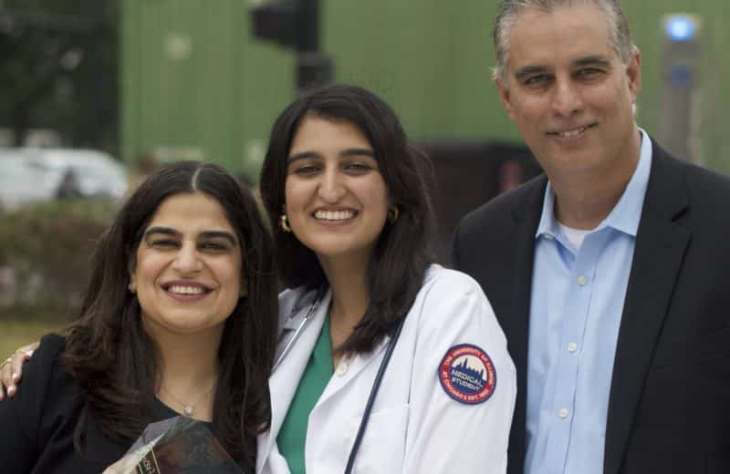 Medical student Hana Ahmed smiles, standing between her parents, at a White Coat Ceremony