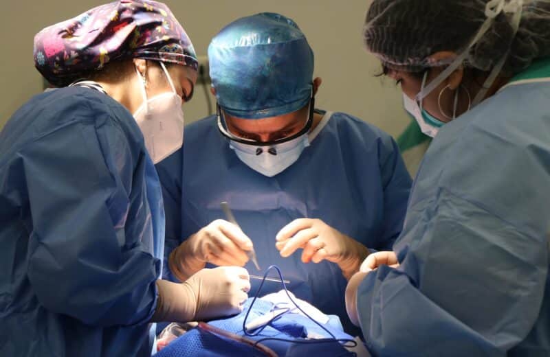 In blue scrubs, a surgical team operates on a patient.