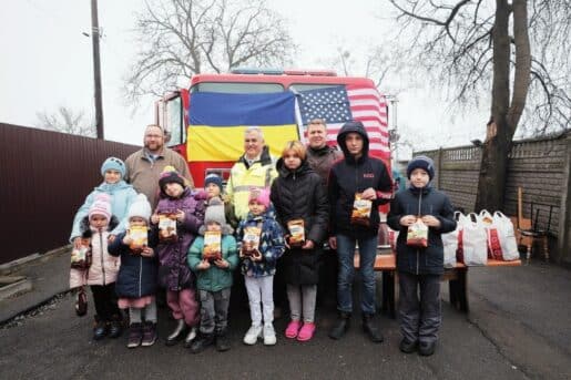 Ukrainian families pose in front of a fire engine draped in U.S. and Ukrainian flags.