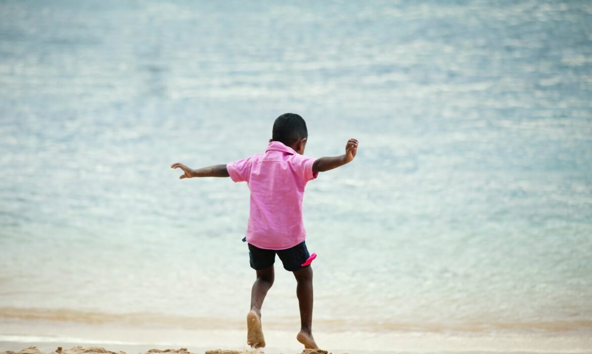 A young boy in a pink t-shirt plays at the water's edge.