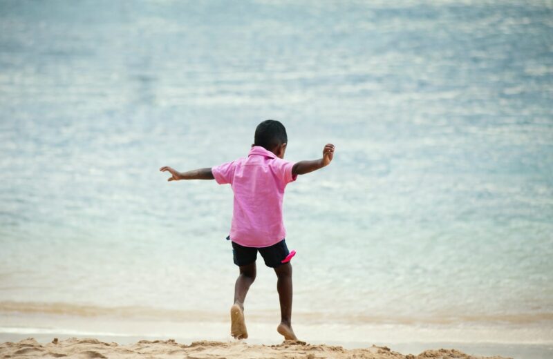 A young boy in a pink t-shirt plays at the water's edge.