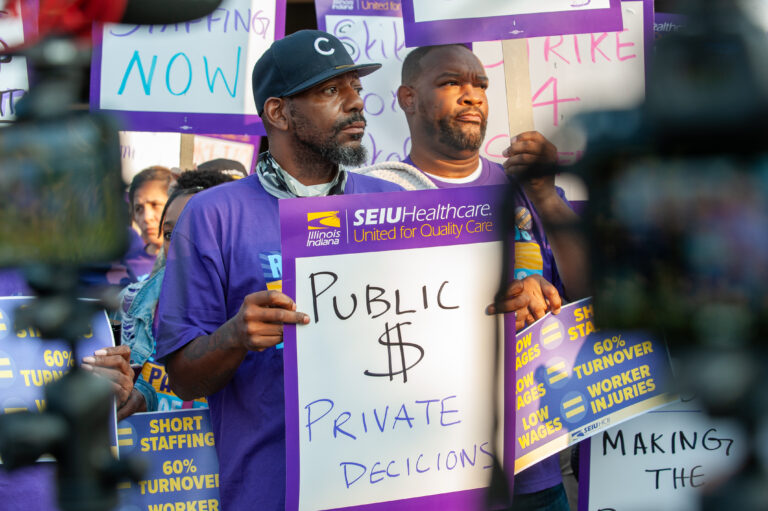 A Loretto Hospital worker in a purple SEIU shirt holds a picket sign that says "Public $ Private Decisions"