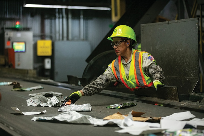 A worker at Groot removes plastics, film, and other contaminants from a fast-moving conveyor belt full of mixed paper