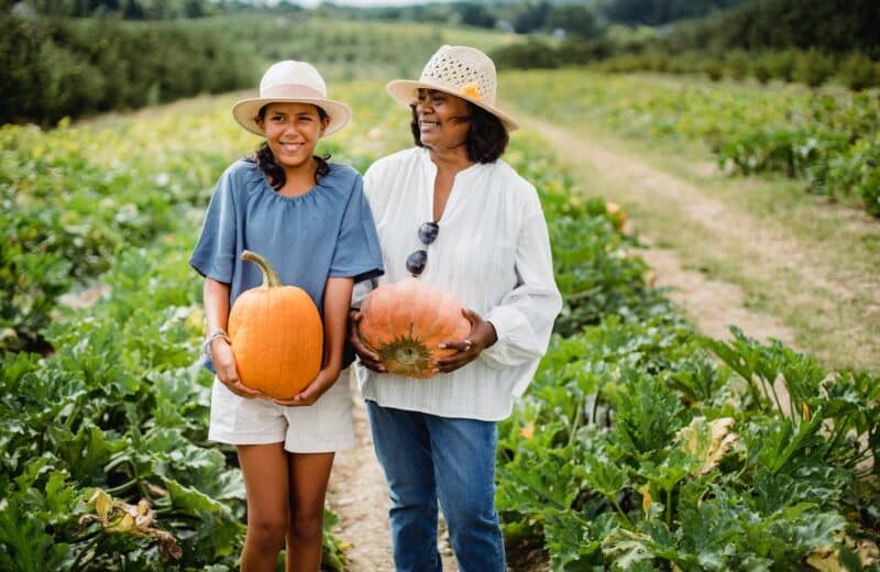 Hispanic daughter and mother carry pumpkins in a pumpkin patch