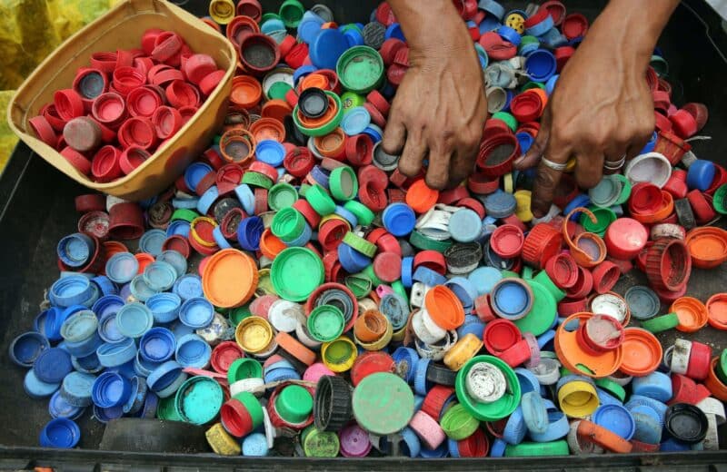 A pair of hands digs through a pile of multi-colored bottle caps.