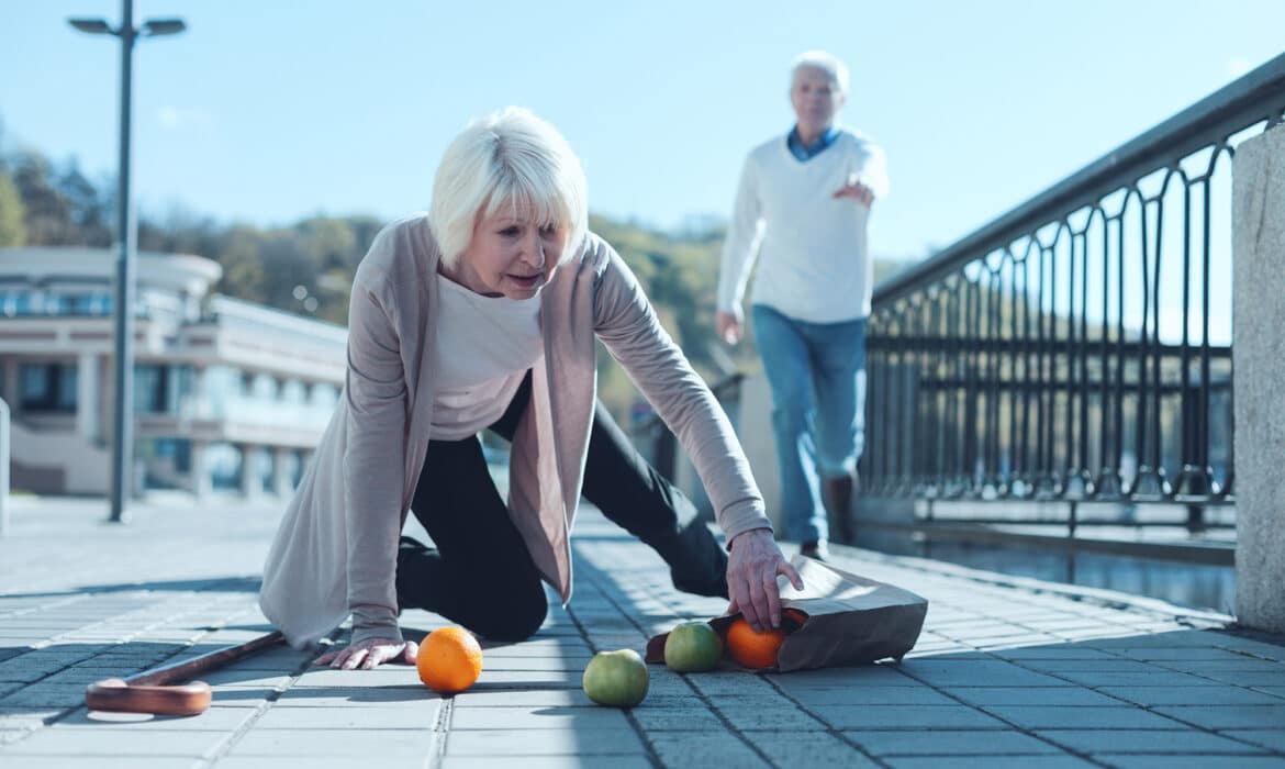 Senior woman kneeling on the ground and picking up her groceries after falling down