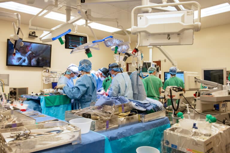 A surgical team in blue scrubs operates over a table.