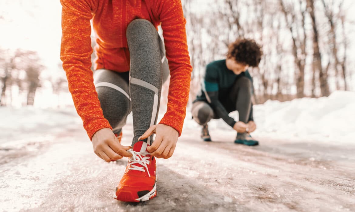 Staying fit during winter, two people lace up their gym shoes on an icy trail. Embracing winter fitness.