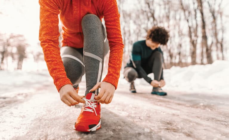 Staying fit during winter, two people lace up their gym shoes on an icy trail. Embracing winter fitness.