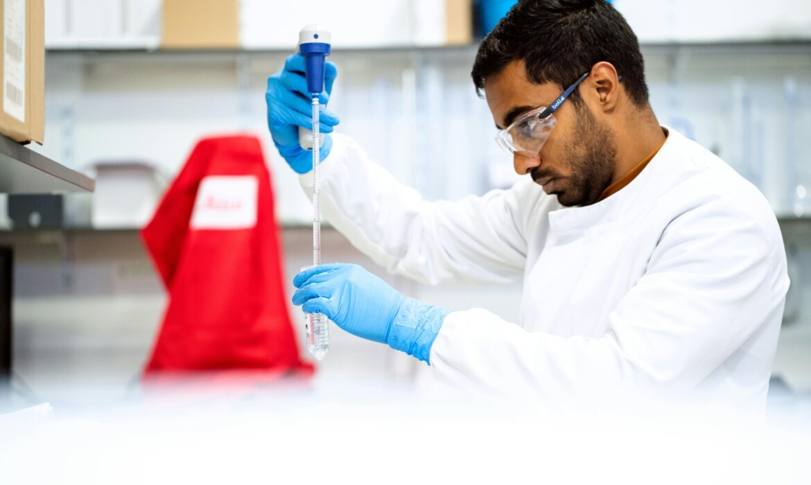 A research wearing goggles uses a pipette to insert a substance into a test tube.