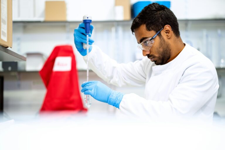 A research wearing goggles uses a pipette to insert a substance into a test tube.