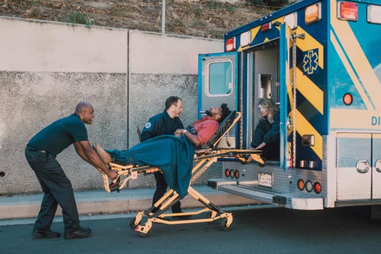 Paramedics load a patient into an ambulance parked on the side of the road.