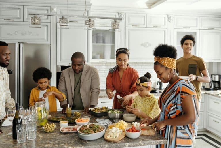 A family gathers around a counter, preparing a meal full of healthy fruits and vegetables.