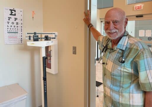 Murray Scheinman, MD, stands beside a height and weight measurement machine and visual chart, smiling.