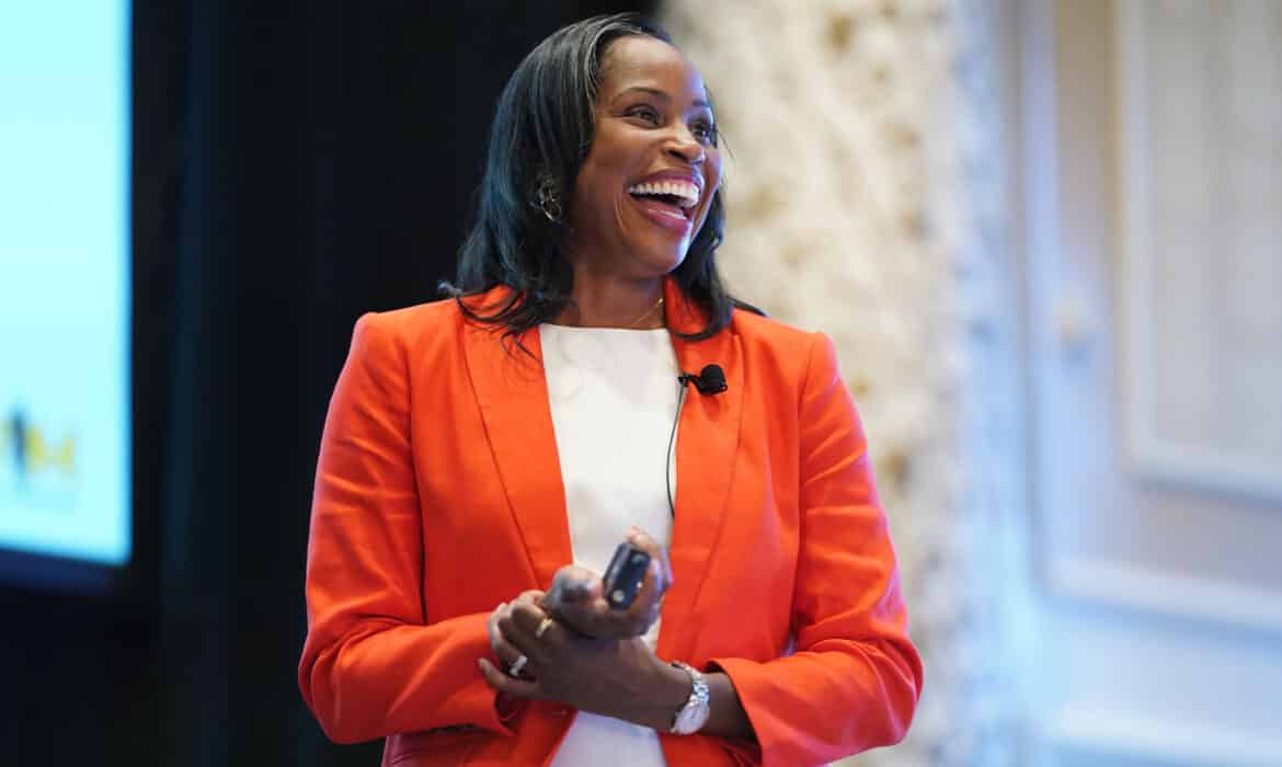 Marcia Faustin, MD, laughs before a crowd at the annual Women in Medicine Summit in Chicago. She's wearing an orange jacket and white shirt.