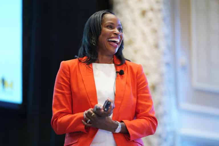 Marcia Faustin, MD, laughs before a crowd at the annual Women in Medicine Summit in Chicago. She's wearing an orange jacket and white shirt.
