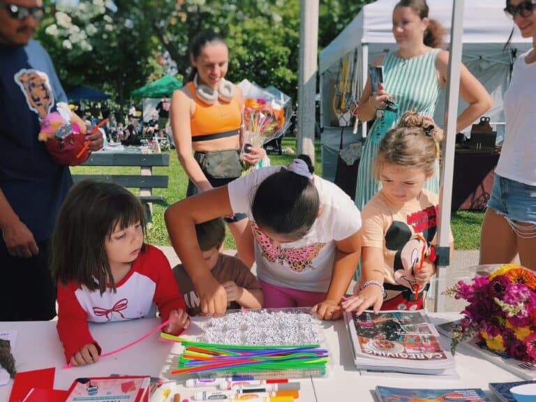 Children at a Chicago farmers market gather around a table for Kid's Lit Day, to make alphabet-bead bracelets.