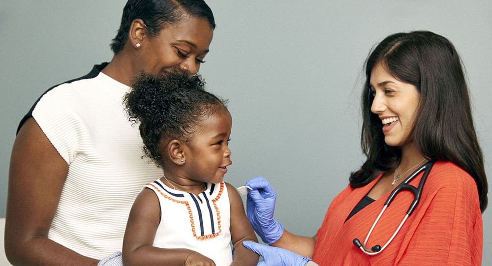 A nurse vaccinates a baby, sitting on mom's lap, against hepatitis B.