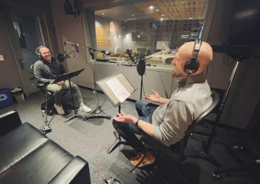 Dan Dean and Ian Hughes sit in a recording studio before microphones.