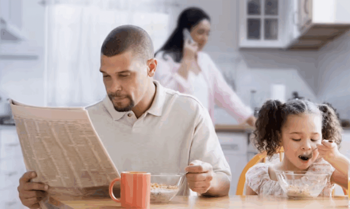 A dad reads the newspaper during breakfast with his daughter