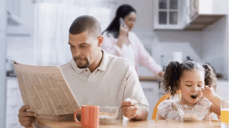 A dad reads the newspaper during breakfast with his daughter