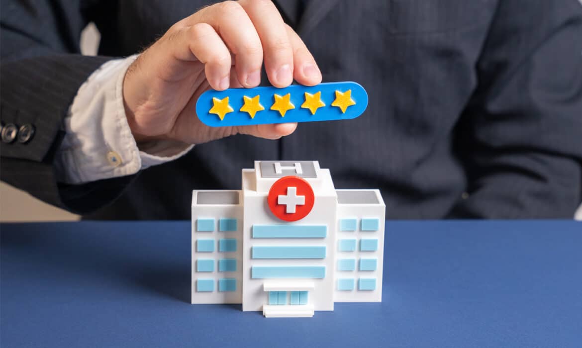 A hand holds 5 stars over a model of a hospital representing the hospital rating system