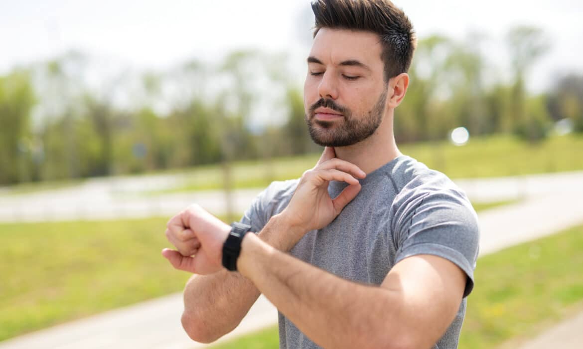 Man checking his pulse as he receives an alert on his smartwatch while jogging outdoors