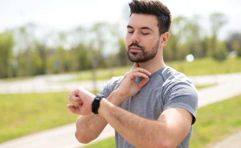 Man checking his pulse as he receives an alert on his smartwatch while jogging outdoors