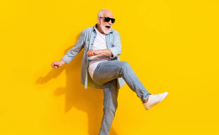 Portrait of an energetic senior man having fun on a yellow sweep wearing sunglasses and dancing