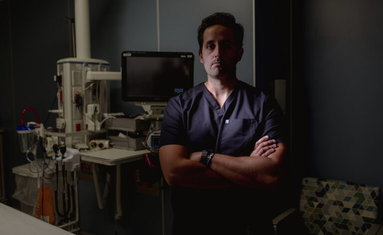 Dark moody portrait of Dr. Nicholas Cozzi, an emergency medicine physician at Rush University Medical Center. He is seen with arms crossed in an operating room. Photo by Jim Vondruska